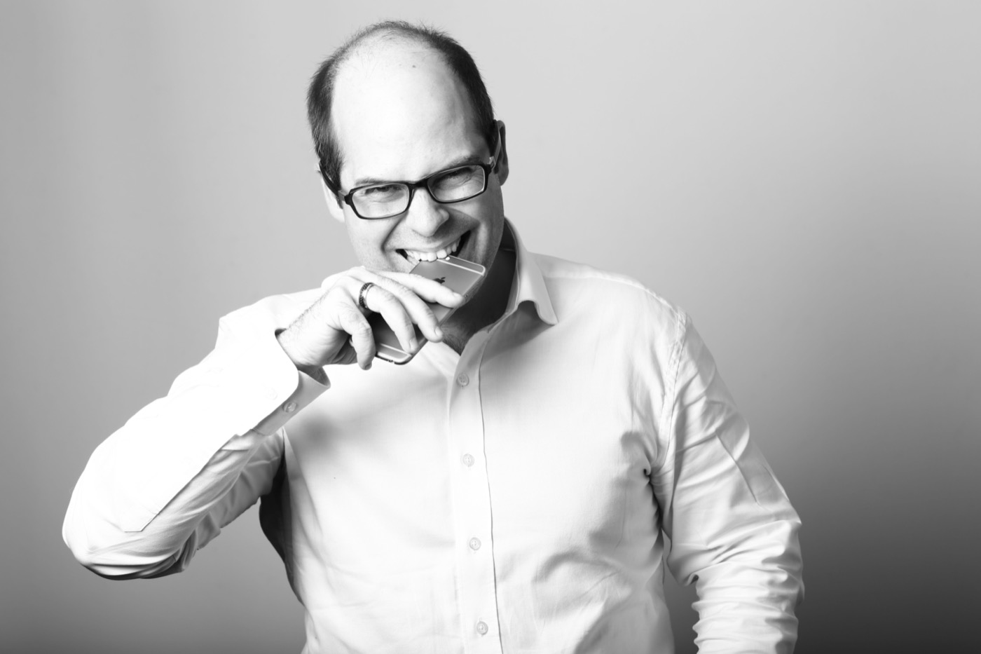 Sébastien Bourguignon, portrait candide en noir et blanc, souriant, tenant un téléphone.